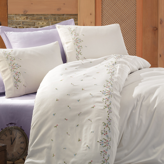 Lilac color bed sheet pairs with white duvet cover that is adorned with colorful floral embroideries